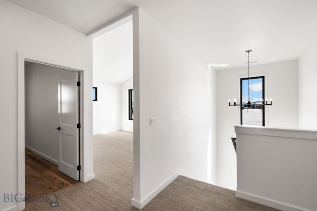 hall with baseboards, a notable chandelier, carpet flooring, and an upstairs landing