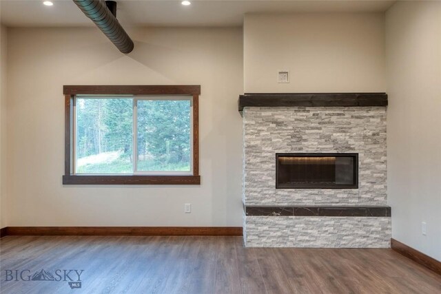 unfurnished living room featuring recessed lighting, wood finished floors, baseboards, and a stone fireplace