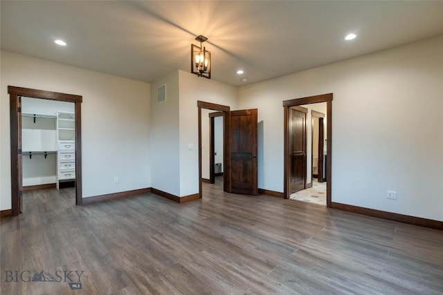 unfurnished bedroom with a spacious closet, dark wood-style floors, visible vents, baseboards, and a chandelier
