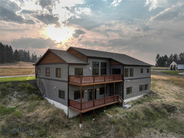 back of property at dusk featuring roof with shingles and a deck