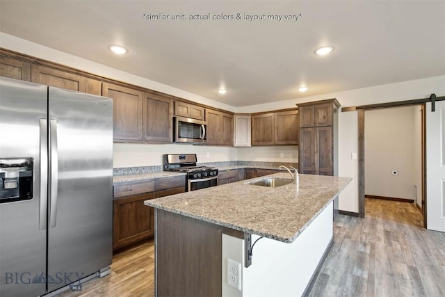 kitchen featuring light wood finished floors, stainless steel appliances, a sink, a barn door, and light stone countertops