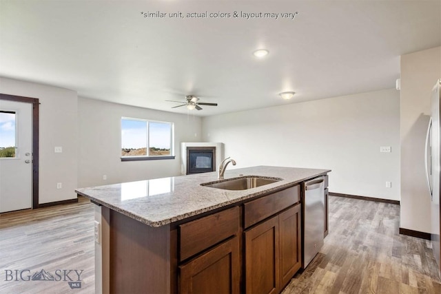 kitchen featuring stainless steel dishwasher, a ceiling fan, a sink, a glass covered fireplace, and light wood-type flooring