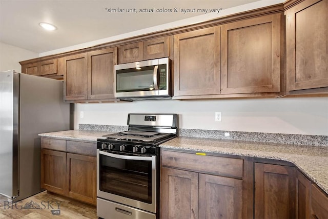 kitchen featuring recessed lighting, light stone counters, light wood-style floors, brown cabinetry, and appliances with stainless steel finishes