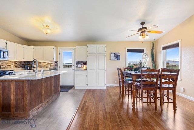 kitchen featuring a ceiling fan, tasteful backsplash, wood finished floors, white cabinets, and stainless steel microwave