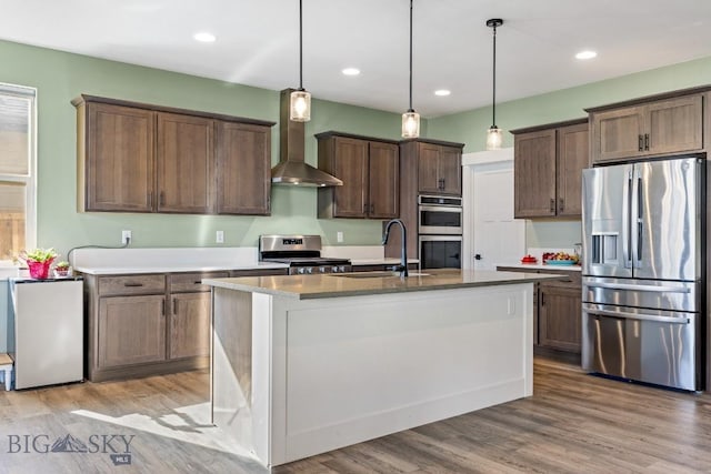 kitchen with pendant lighting, wall chimney range hood, a sink, light wood-style flooring, and stainless steel appliances