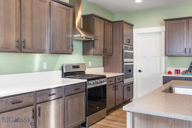 kitchen featuring light countertops, appliances with stainless steel finishes, and wall chimney range hood