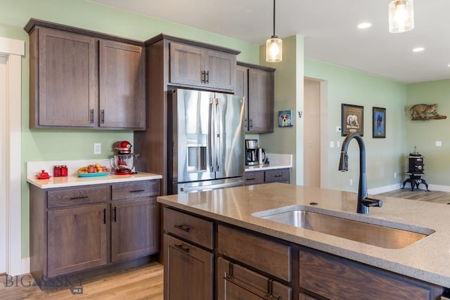kitchen with hanging light fixtures, stainless steel fridge, a sink, and light wood-type flooring