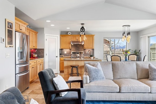 1708 Drummond Blvd, Belgrade, MT 59714 - kitchen featuring stainless steel refrigerator with ice dispenser, open floor plan, under cabinet range hood, light brown cabinets, and lofted ceiling