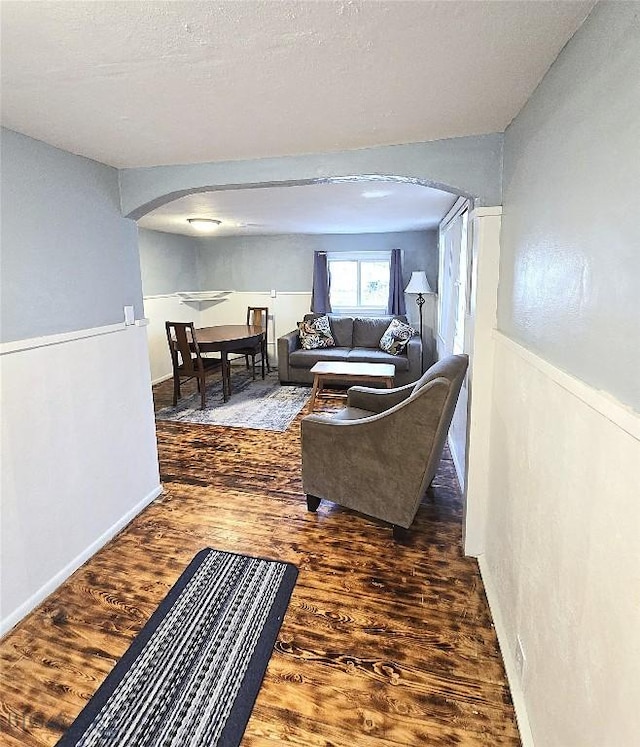 living area featuring arched walkways, wood finished floors, and baseboards