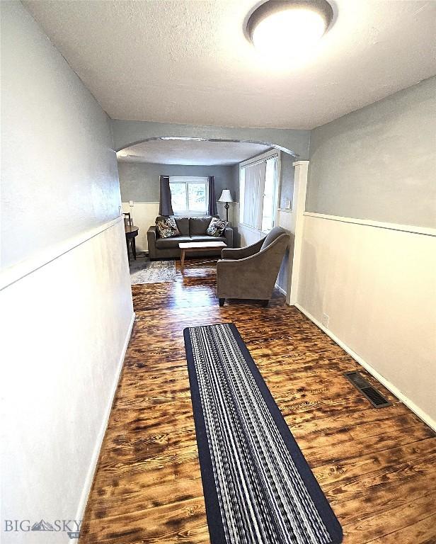 hall with arched walkways, wood finished floors, visible vents, and baseboards