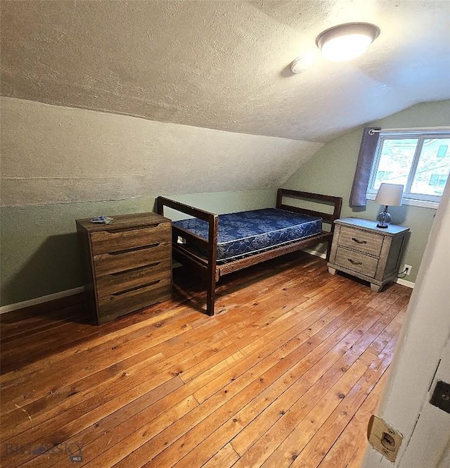 bedroom with light wood finished floors, vaulted ceiling, and a textured ceiling