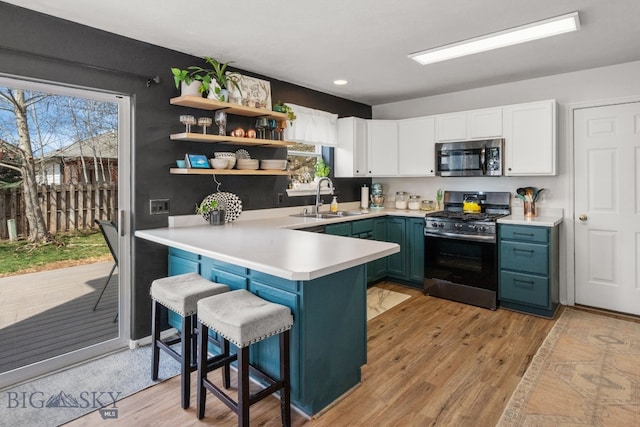 kitchen with a sink, light wood-type flooring, a peninsula, appliances with stainless steel finishes, and white cabinetry