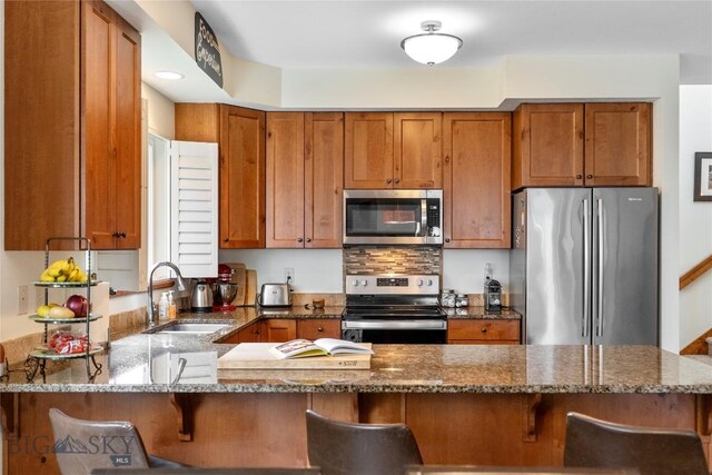 268 Pine Creek Dr, Bozeman, MT 59718 - kitchen featuring a kitchen breakfast bar, dark stone countertops, a sink, brown cabinetry, and appliances with stainless steel finishes