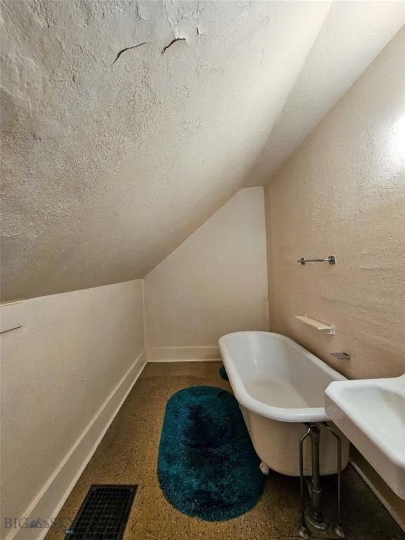 602 Harris, Big Timber, MT 59011 - bathroom featuring a soaking tub, a textured ceiling, vaulted ceiling, visible vents, and a textured wall