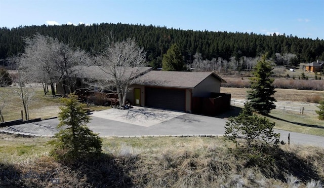 exterior space featuring driveway, fence, a view of trees, and a garage
