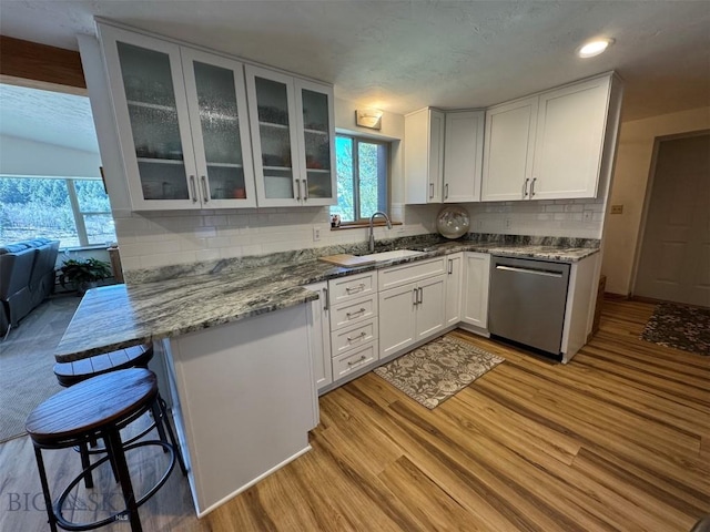kitchen featuring white cabinets, backsplash, dishwasher, light wood finished floors, and a sink