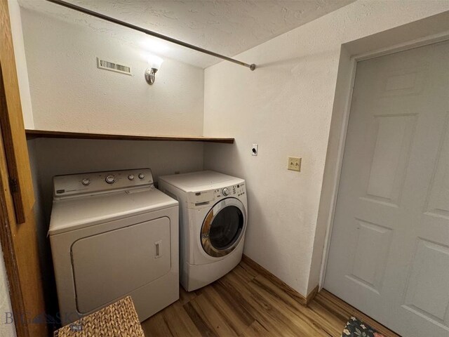 laundry room with visible vents, light wood-type flooring, washing machine and clothes dryer, and baseboards