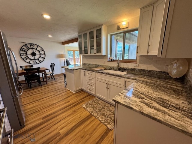 kitchen with light wood finished floors, a sink, white cabinets, and freestanding refrigerator
