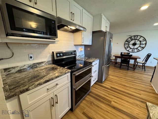 kitchen featuring tasteful backsplash, white cabinets, appliances with stainless steel finishes, light wood-style floors, and under cabinet range hood