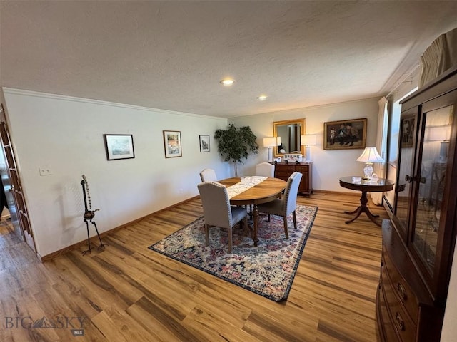 dining area with baseboards, ornamental molding, a textured ceiling, and wood finished floors