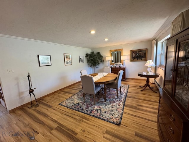 dining area with baseboards, ornamental molding, a textured ceiling, and wood finished floors