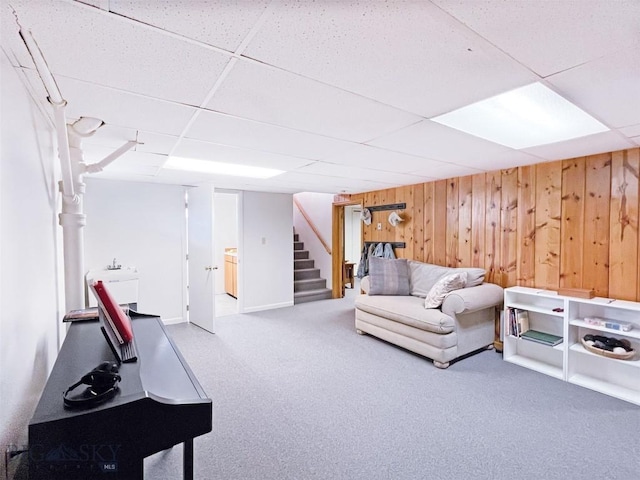 sitting room featuring stairway, wooden walls, a paneled ceiling, and carpet floors
