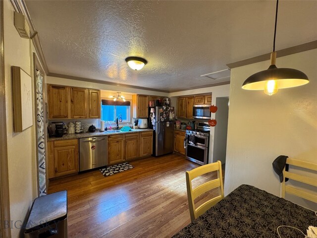 kitchen featuring brown cabinetry, stainless steel appliances, dark wood-style flooring, a sink, and crown molding