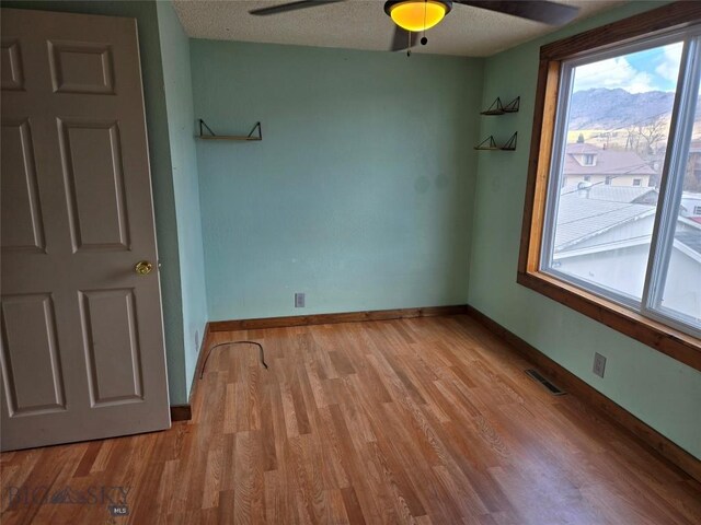 spare room featuring light wood finished floors, visible vents, ceiling fan, and baseboards