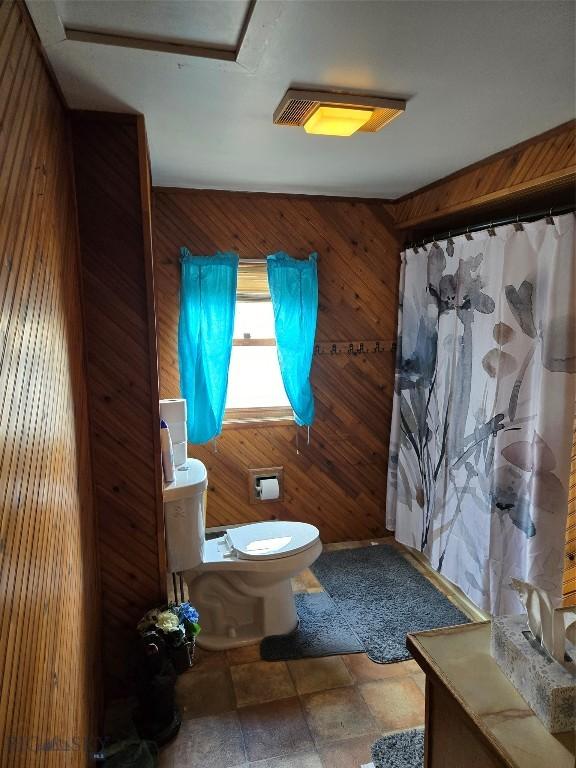 full bath featuring toilet, a shower with curtain, wooden walls, and stone finish flooring