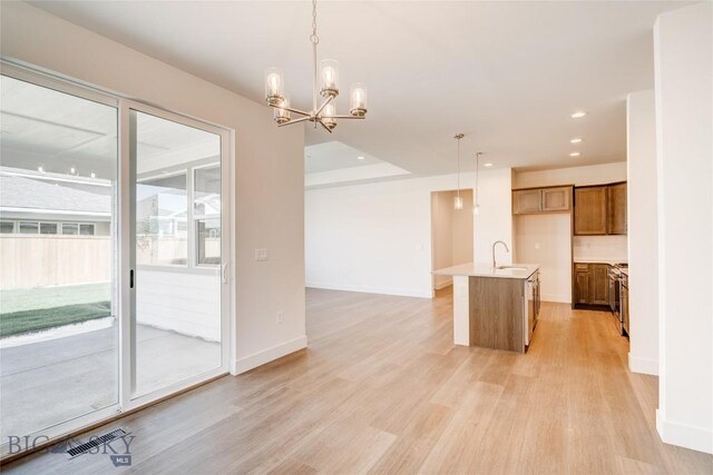 1520 Cyril Way, Belgrade, MT 59714 - kitchen with brown cabinets, light wood finished floors, decorative light fixtures, a chandelier, and a center island with sink