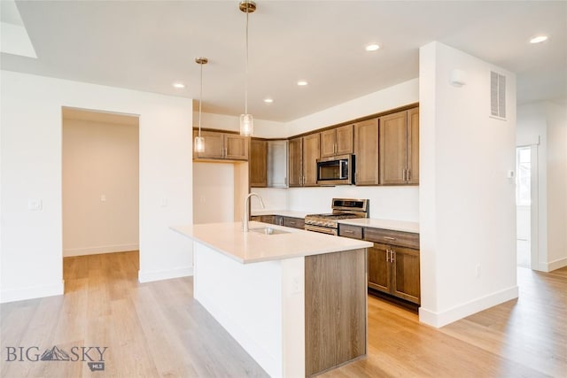 1520 Cyril Way, Belgrade, MT 59714 - kitchen featuring stainless steel appliances, light wood-style flooring, hanging light fixtures, a center island with sink, and light countertops