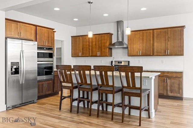1511 Masterson, Belgrade, MT 59714 - kitchen featuring a kitchen island with sink, decorative backsplash, light wood-style floors, appliances with stainless steel finishes, and wall chimney exhaust hood