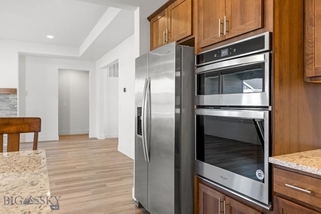 1511 Masterson, Belgrade, MT 59714 - kitchen featuring stainless steel appliances, brown cabinets, light wood-style flooring, light stone countertops, and a raised ceiling