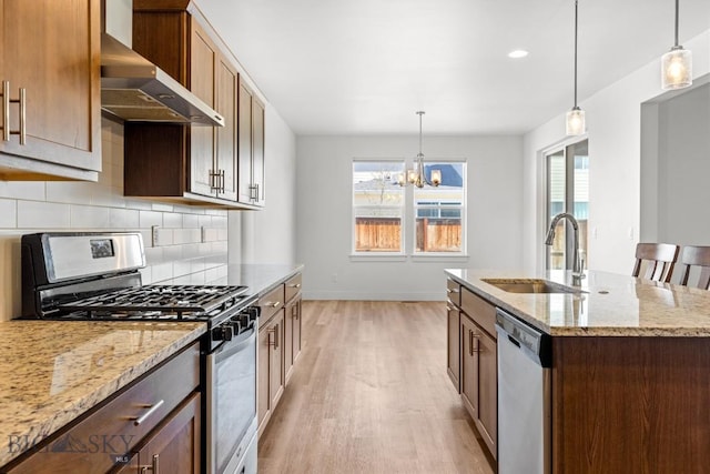 1511 Masterson, Belgrade, MT 59714 - kitchen with stainless steel appliances, wall chimney range hood, light wood finished floors, backsplash, and a kitchen island with sink