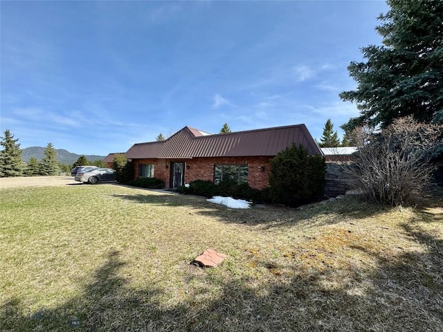 view of side of property with a lawn, a standing seam roof, metal roof, and brick siding