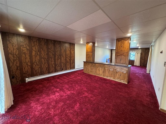 below grade area with dark carpet, a paneled ceiling, and a baseboard radiator