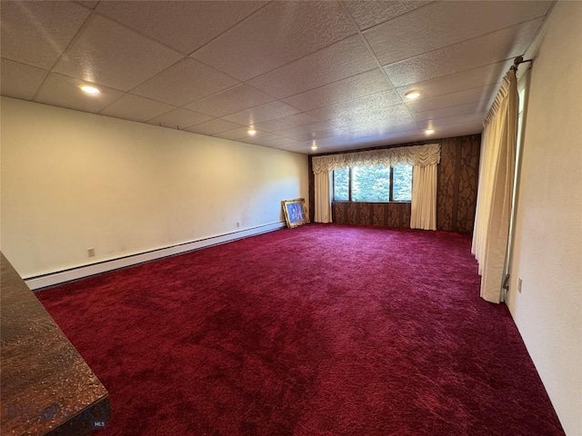 carpeted empty room featuring a drop ceiling and a baseboard radiator