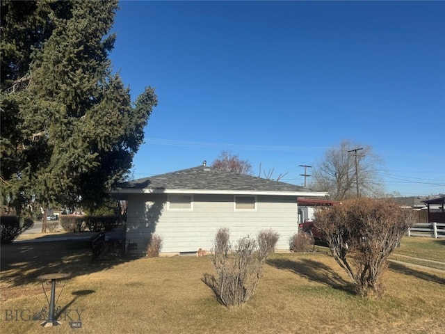 view of side of home featuring fence, roof with shingles, and a lawn