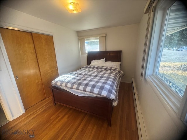 bedroom with a baseboard heating unit, a closet, and wood finished floors