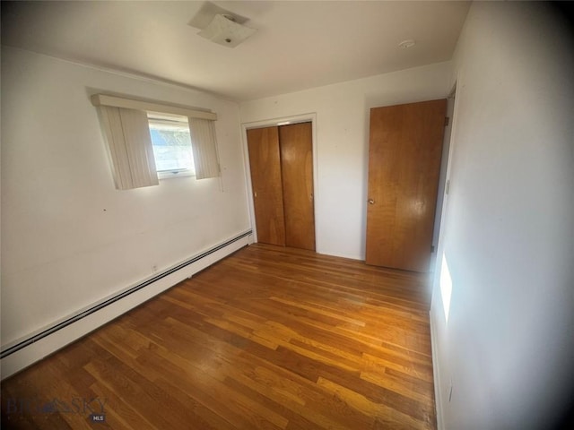 unfurnished bedroom featuring a closet, wood finished floors, and a baseboard radiator