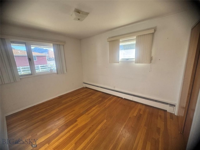 spare room with baseboards, wood finished floors, and a baseboard radiator