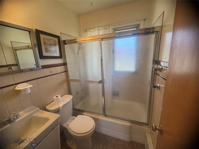 full bath featuring wainscoting, tile walls, toilet, vanity, and bath / shower combo with glass door