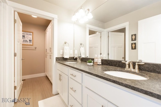 full bath featuring double vanity, wood finished floors, baseboards, and a sink