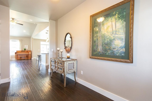 hallway featuring lofted ceiling, dark wood-style floors, and baseboards