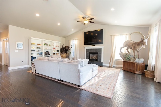 living area featuring a tile fireplace, a ceiling fan, vaulted ceiling, baseboards, and dark wood finished floors