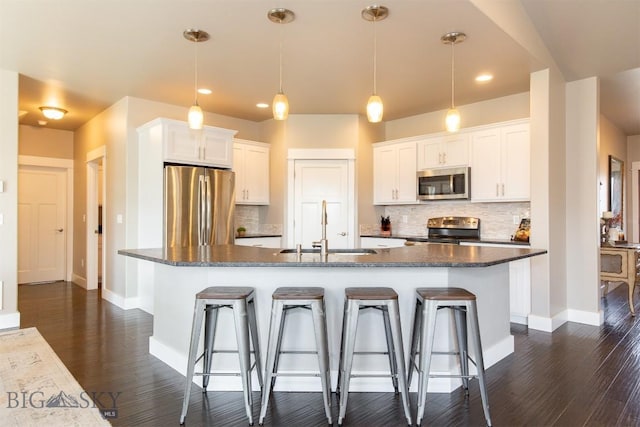 kitchen with a breakfast bar, stainless steel appliances, white cabinets, a sink, and baseboards
