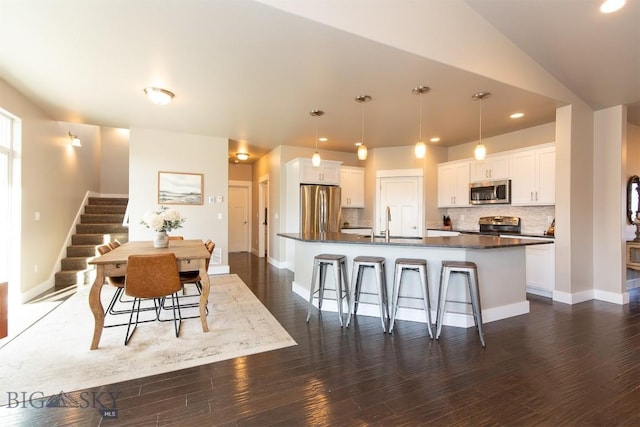 kitchen featuring stainless steel appliances, dark countertops, a kitchen bar, baseboards, and a center island with sink