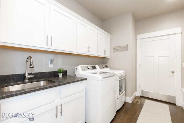 clothes washing area with dark wood-type flooring, washing machine and dryer, cabinet space, and a sink