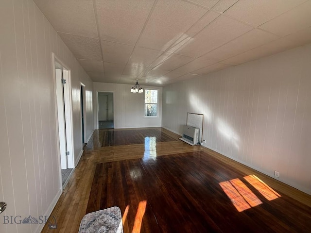 spare room with wood-type flooring, heating unit, a notable chandelier, wood walls, and baseboards