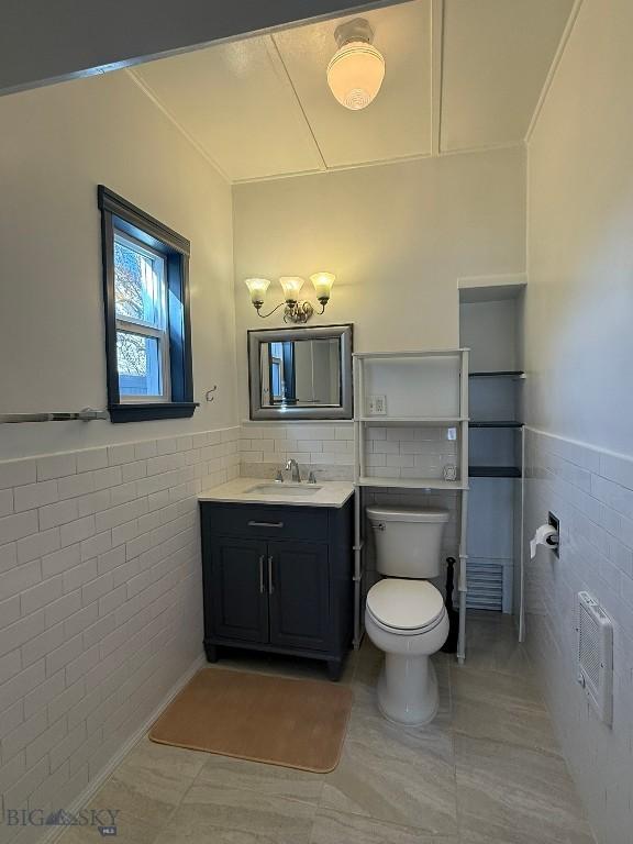 bathroom with heating unit, tile walls, toilet, vanity, and a notable chandelier